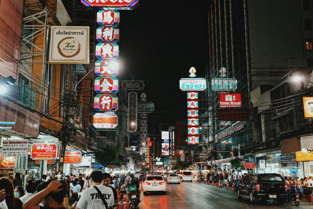 Bustling night scene in Bangkok's Chinatown with illuminated signs, people, and traffic.