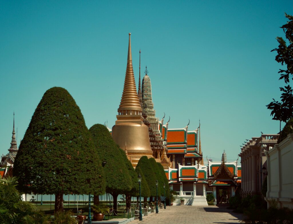 A serene view of a golden stupa in a Thai temple garden with manicured trees and traditional architecture.